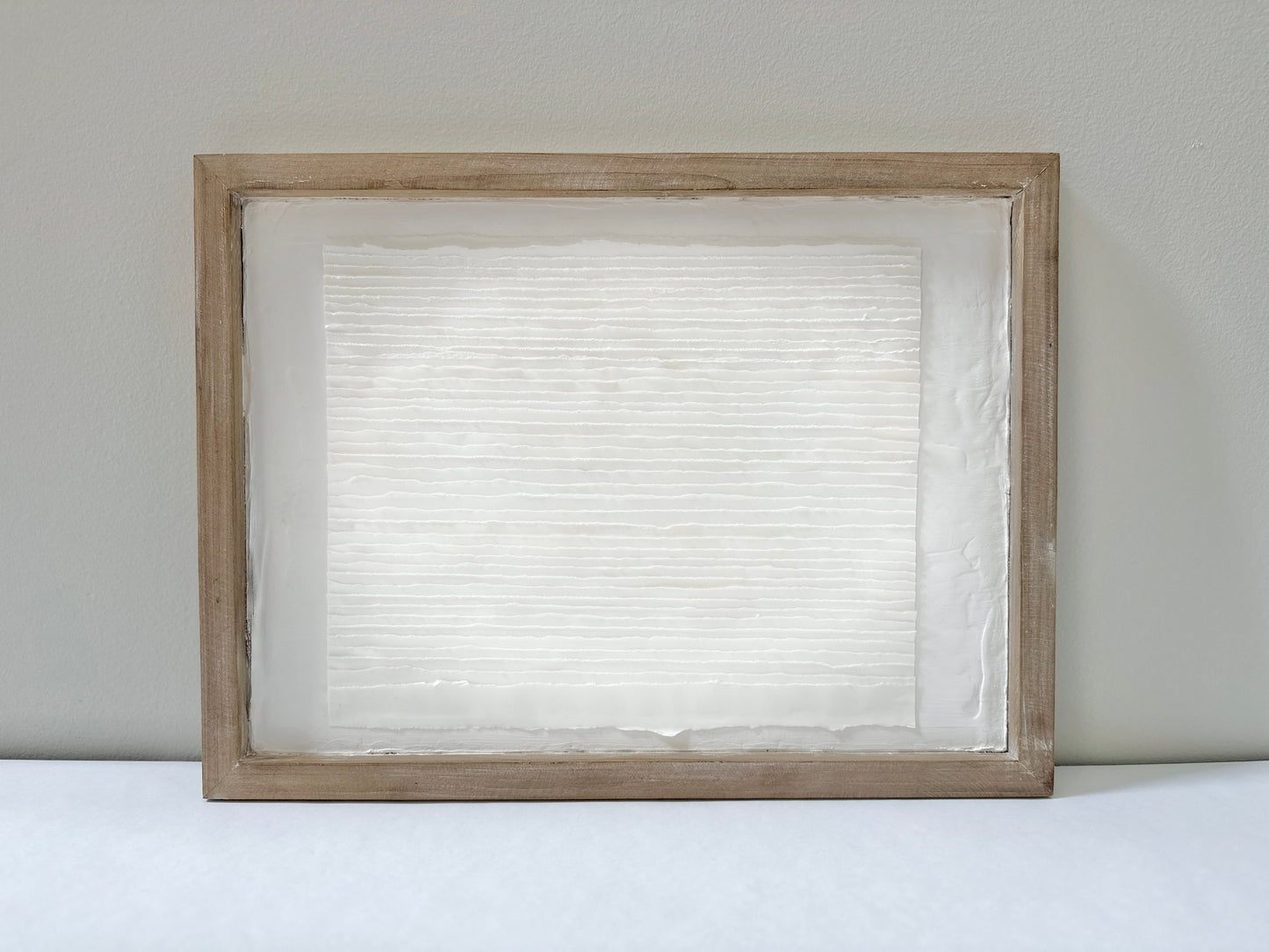 White textured art in a wooden frame against a white wall. Original abstract art by artist Tam M Olson