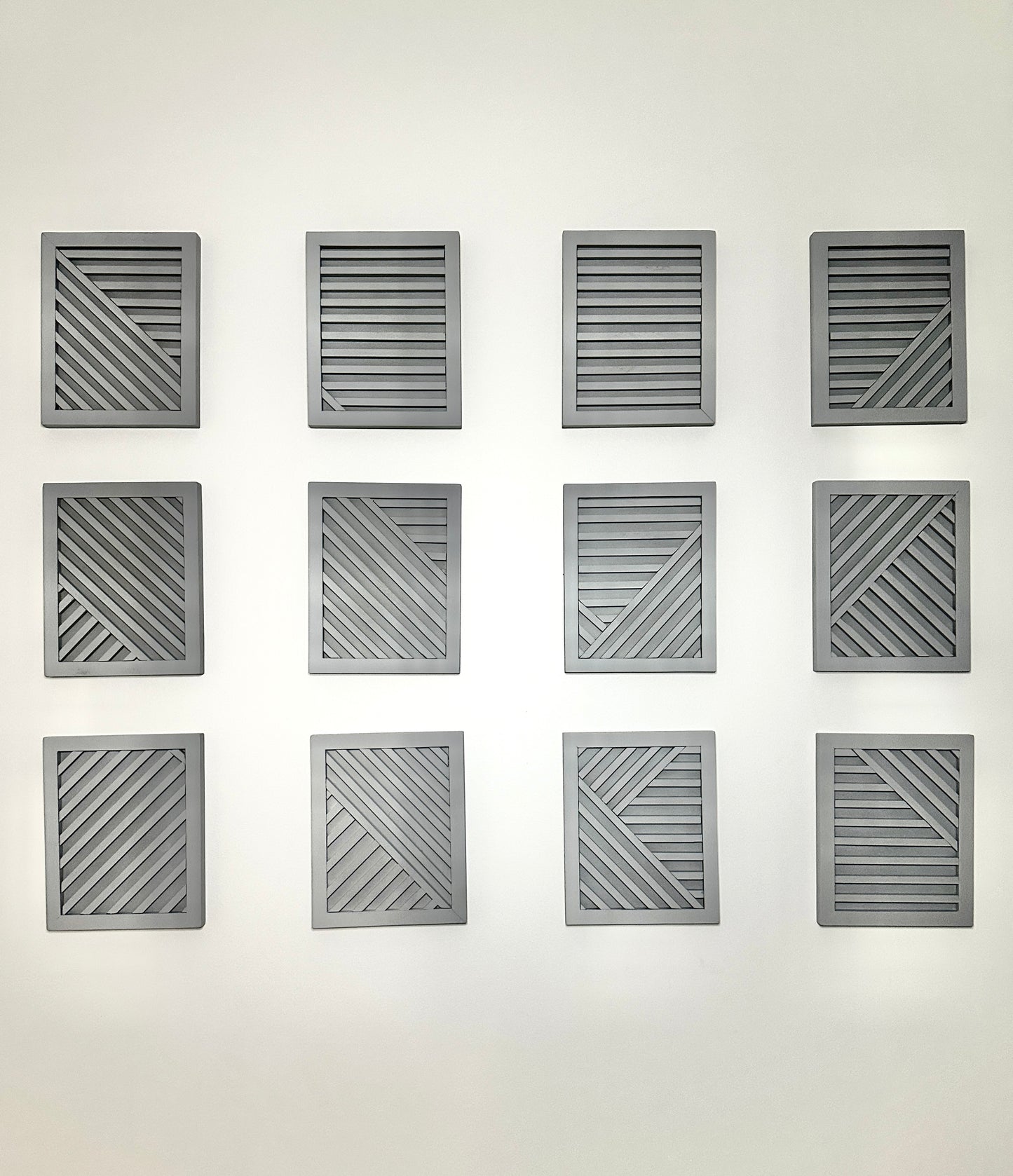 Twelve gray geometric wall art panels on a white wall. Original Commercial Art by Tam M Olson