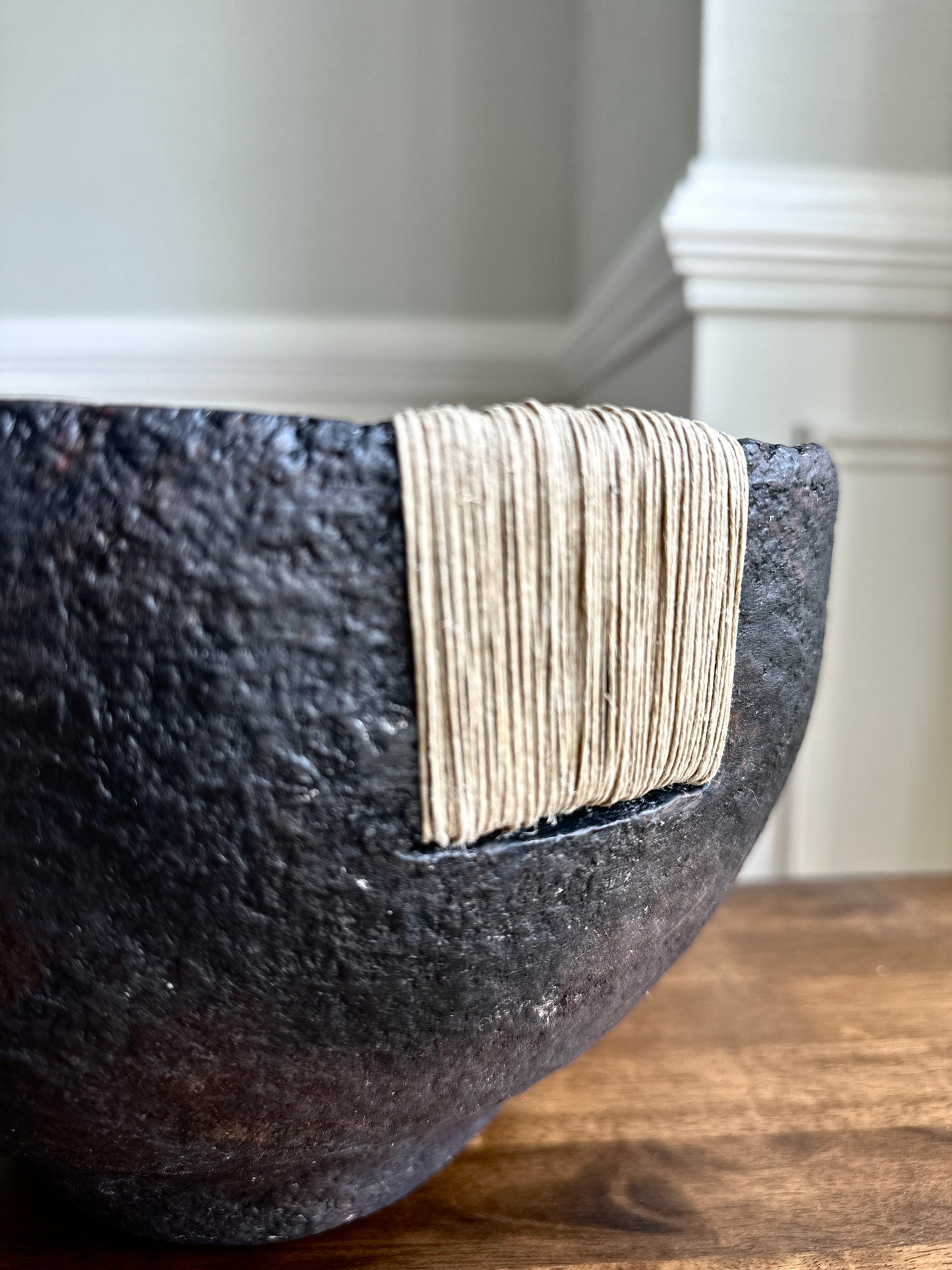 close up of black textural bowl with deep brown patina finish and jute twine accent sitting on a wooden surface. Handcrafted paper mache decorative bowl by Artist Tam M Olson.