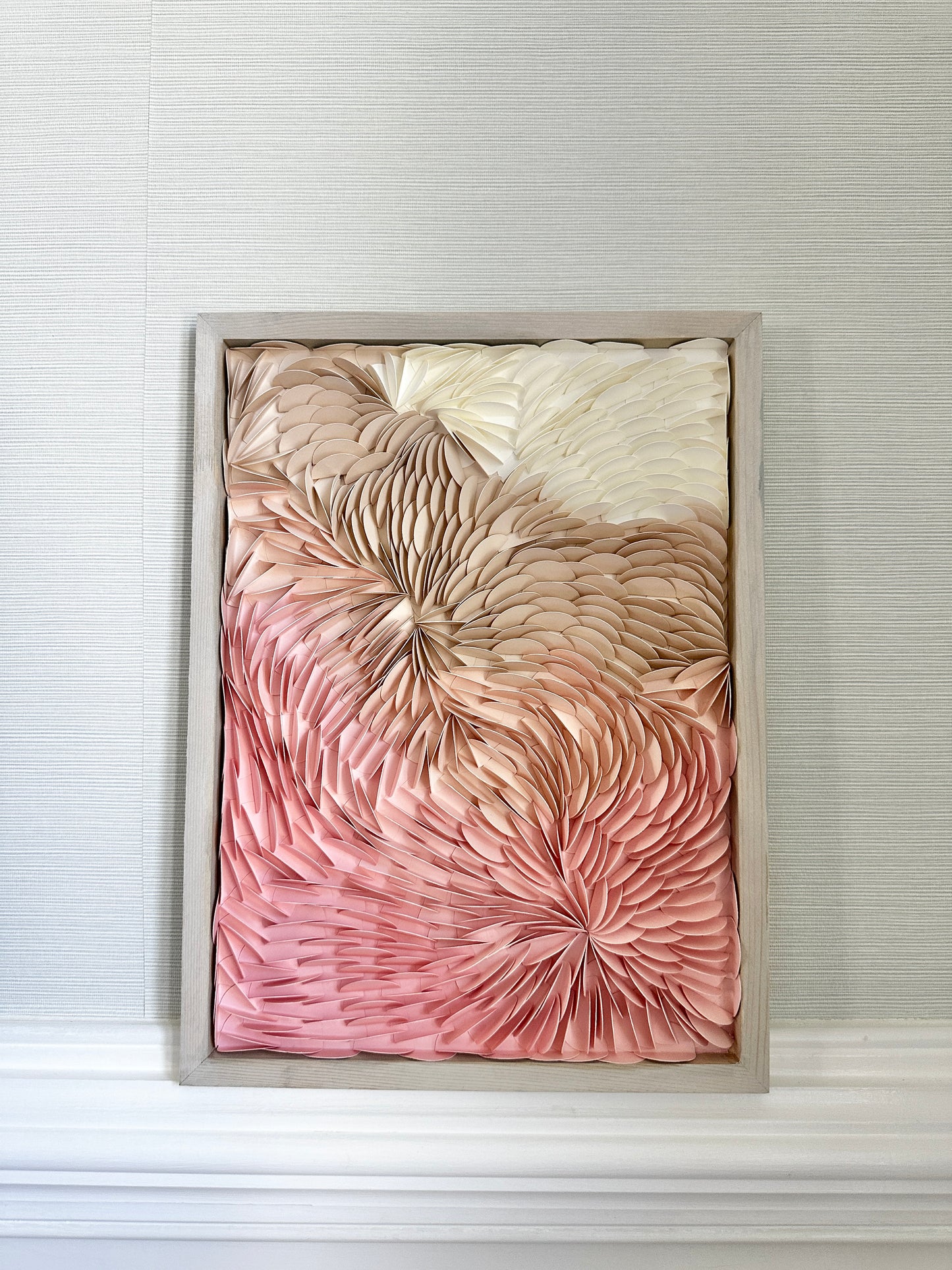 Original framed, textured, origami wall art featuring shades of pink, nudes, beiges and white, displayed in a wooden frame.