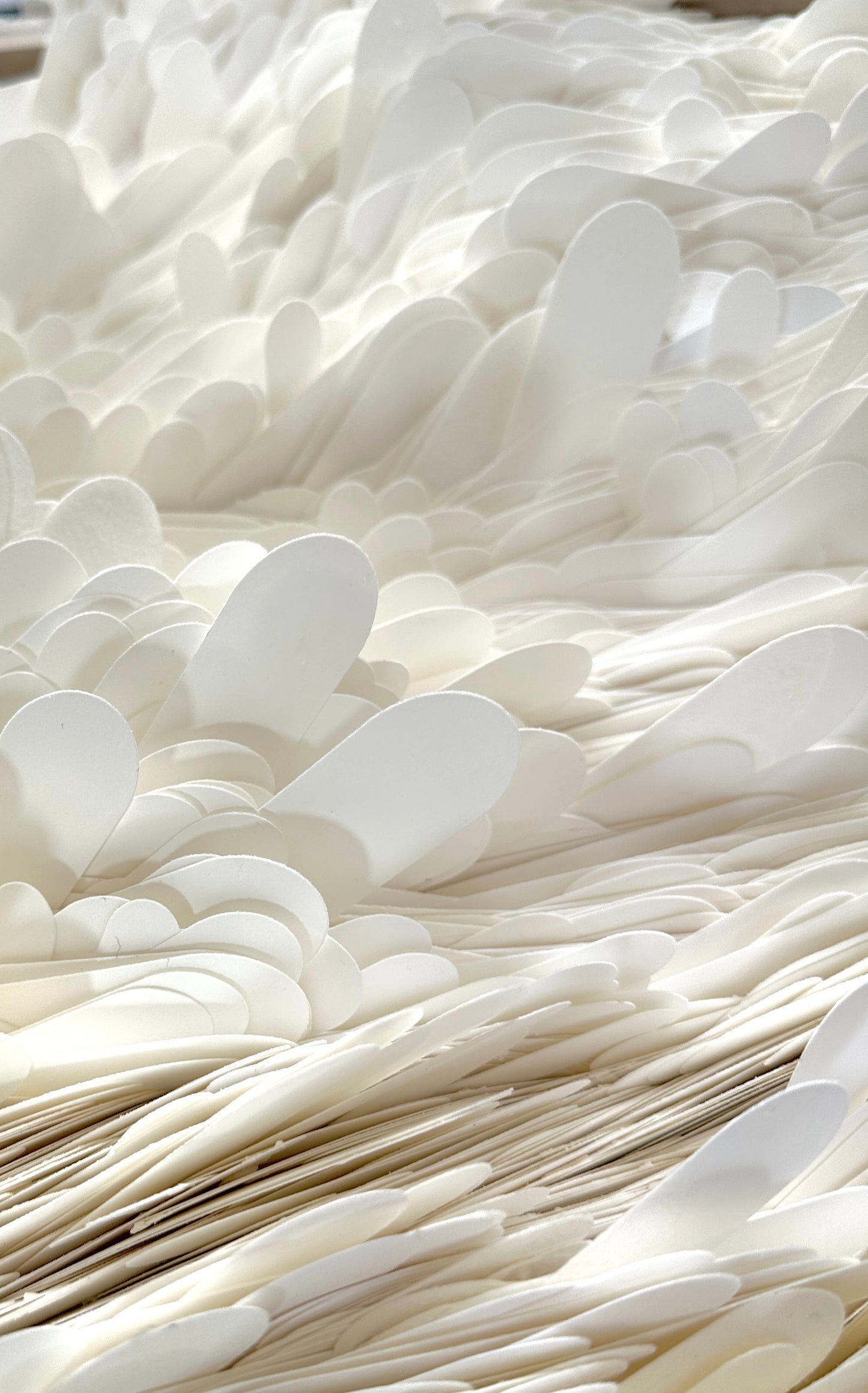 A close-up view of a large quantity of white cardstock fins stacked and layered together, filling the entire frame. Original art by Artist Tam M Olson