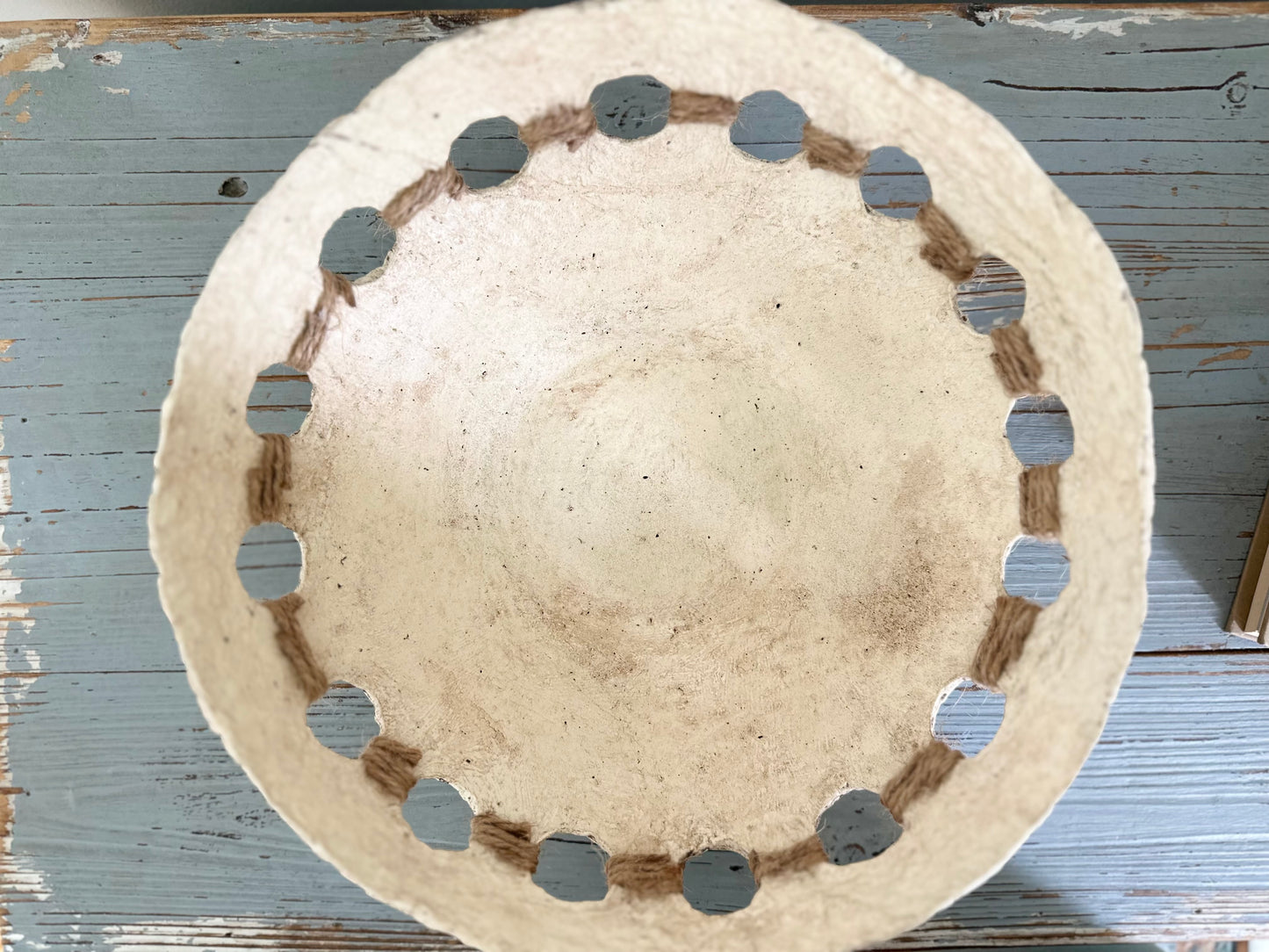 top down view of a beige, primitive handmade paper mache bowl with jute string accents on the side, placed on a flat surface. Designed by Artist Tam M Olson.