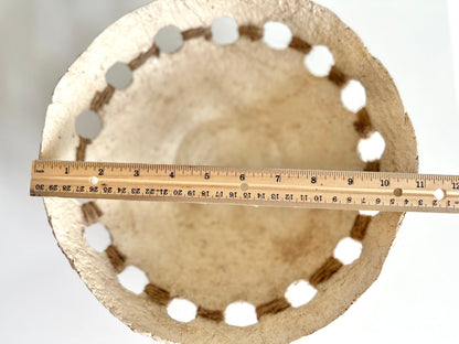 Top down view of a beige, primitive handmade paper mache bowl with jute string accents on the side, placed on a flat surface. Displays bowl width of 11 inches. Designed by Artist Tam M Olson.
