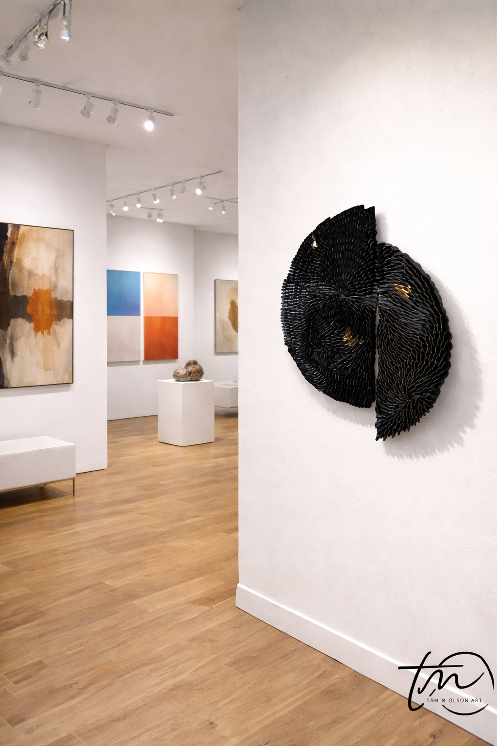 Art gallery with a black abstract sculpture on a white wall and colorful paintings in the background. Original textured abstract wall art by Artist Tam M Olson