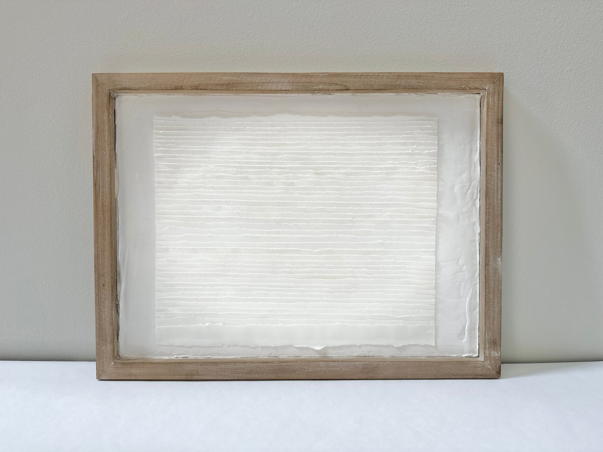 White textured art in a wooden frame against a white wall. Original abstract art by artist Tam M Olson