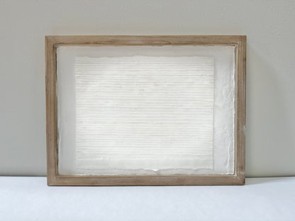 White textured art in a wooden frame against a white wall. Original abstract art by artist Tam M Olson