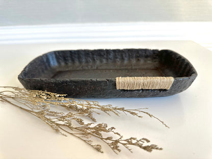 A small black decorative tray with a textured surface, made from paper mache, with jute string detail. Original art by artist Tam M Olson
