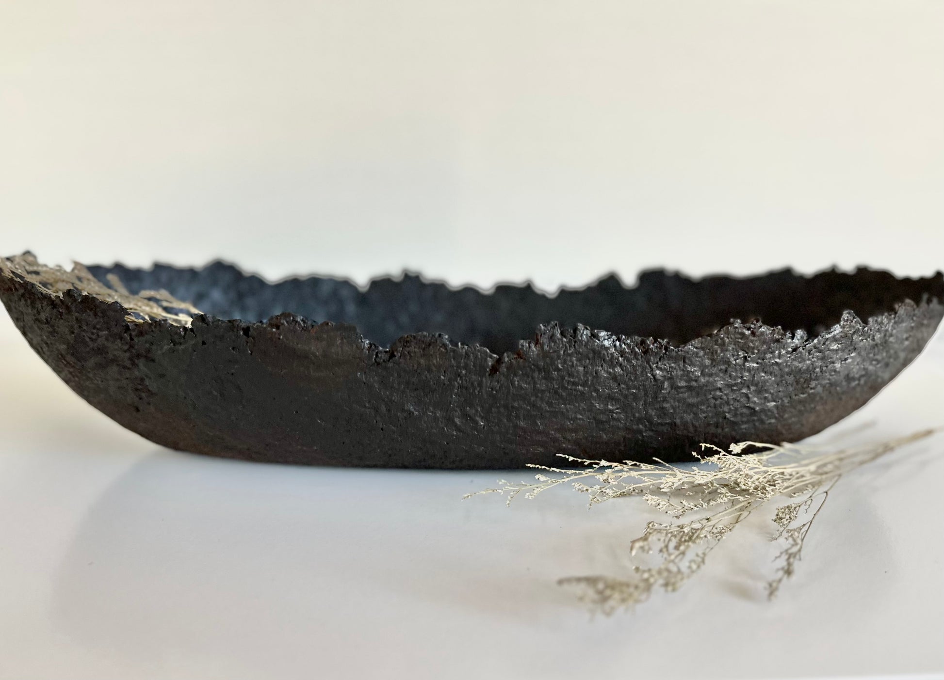 Oblong black textured decorative bowl with irregular edges on white surface. Handmade Paper Mache design by Artist Tam M Olson