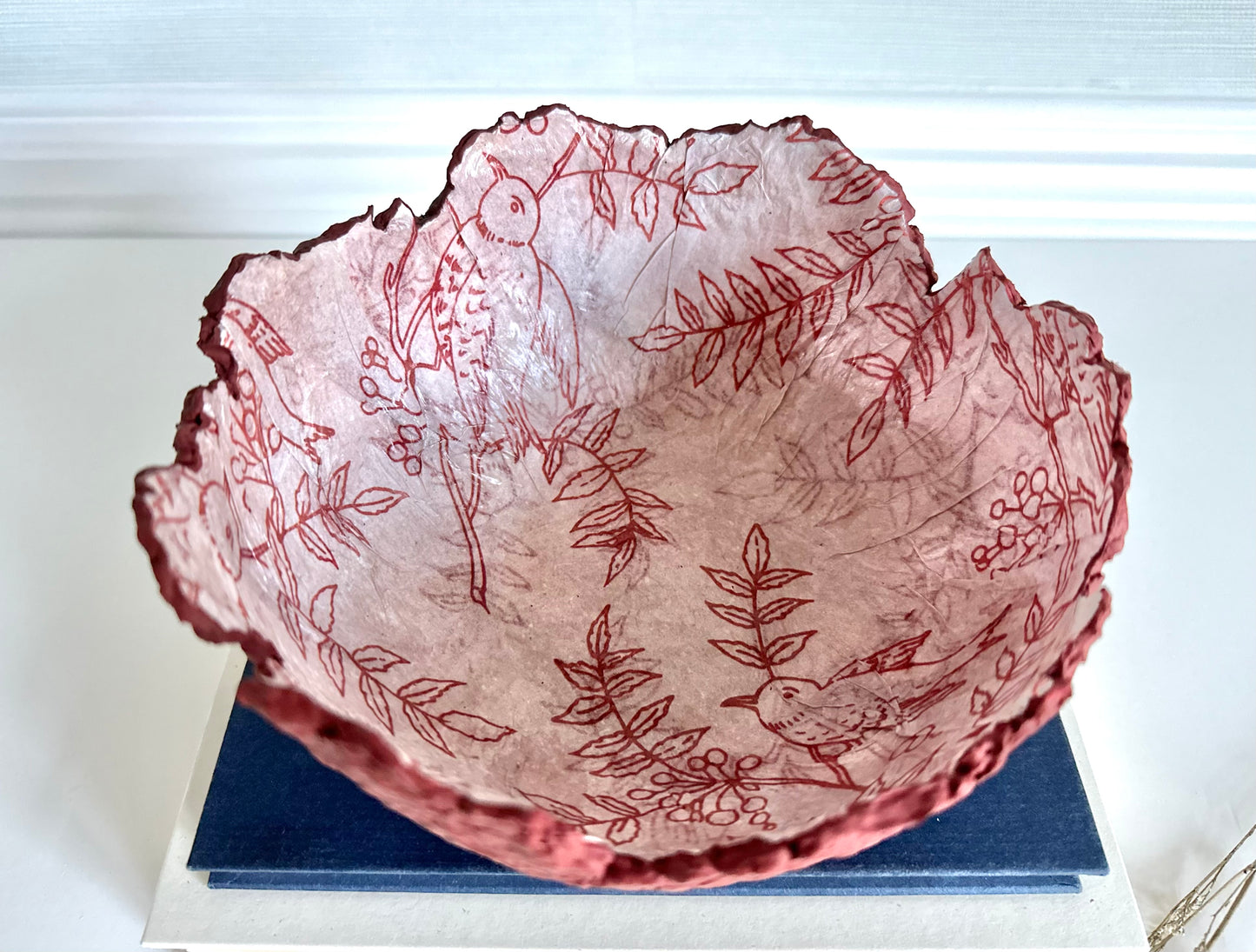 Top down view of a maroon eggshell decorative bowl with a rough torn edge, displaying an interior of birds and branches. Handcrafted by artist Tam M Olson.
