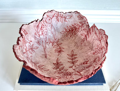 Top down view of a maroon eggshell decorative bowl with a rough torn edge, displaying an interior of birds and branches. Handcrafted by artist Tam M Olson.