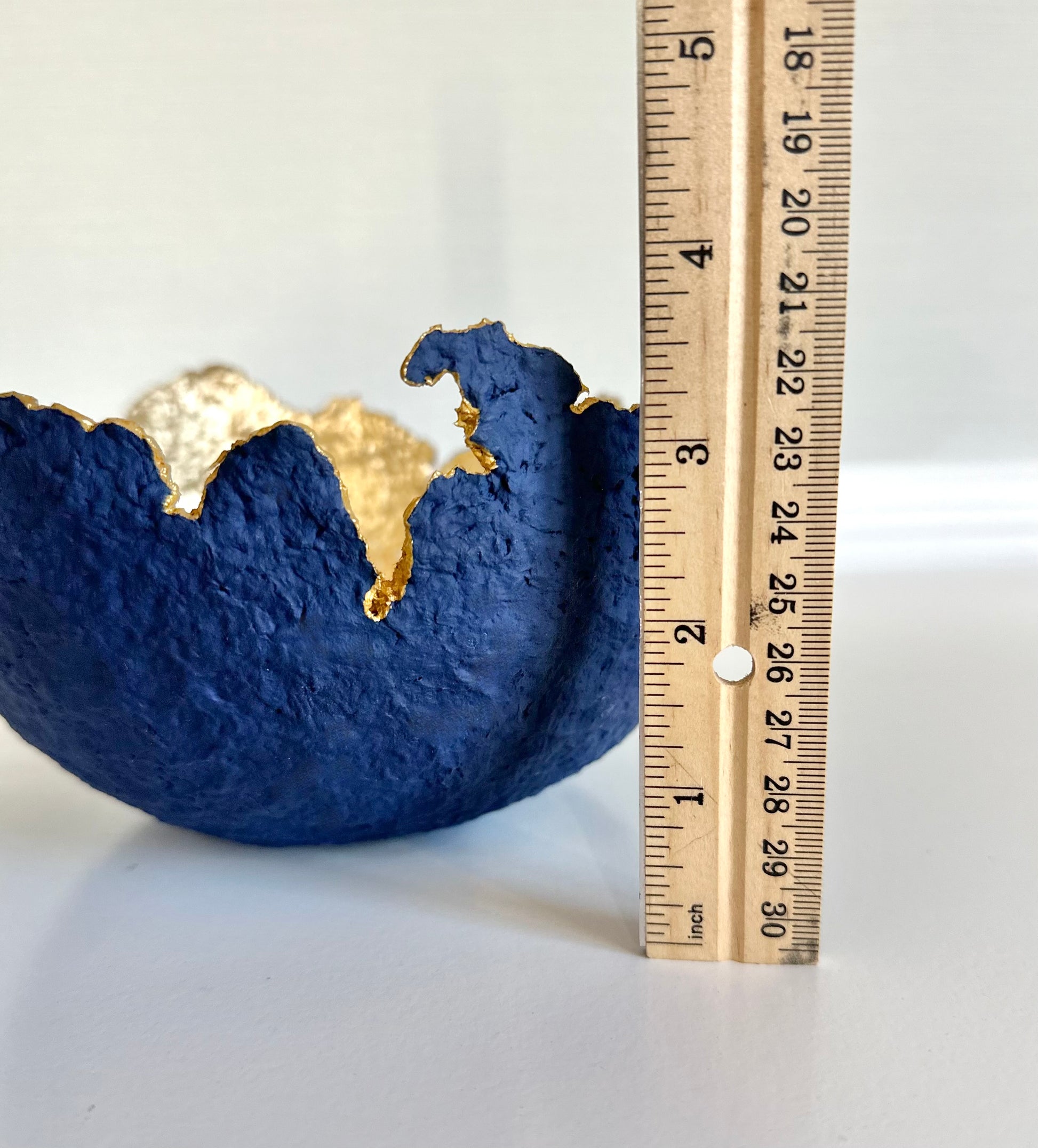 A navy blue paper mache bowl with a gold interior, designed to resemble an eggshell, with ruler nearby to showcase height of nearly 4 inches. Original sculptural bowl by Artist Tam M Olson