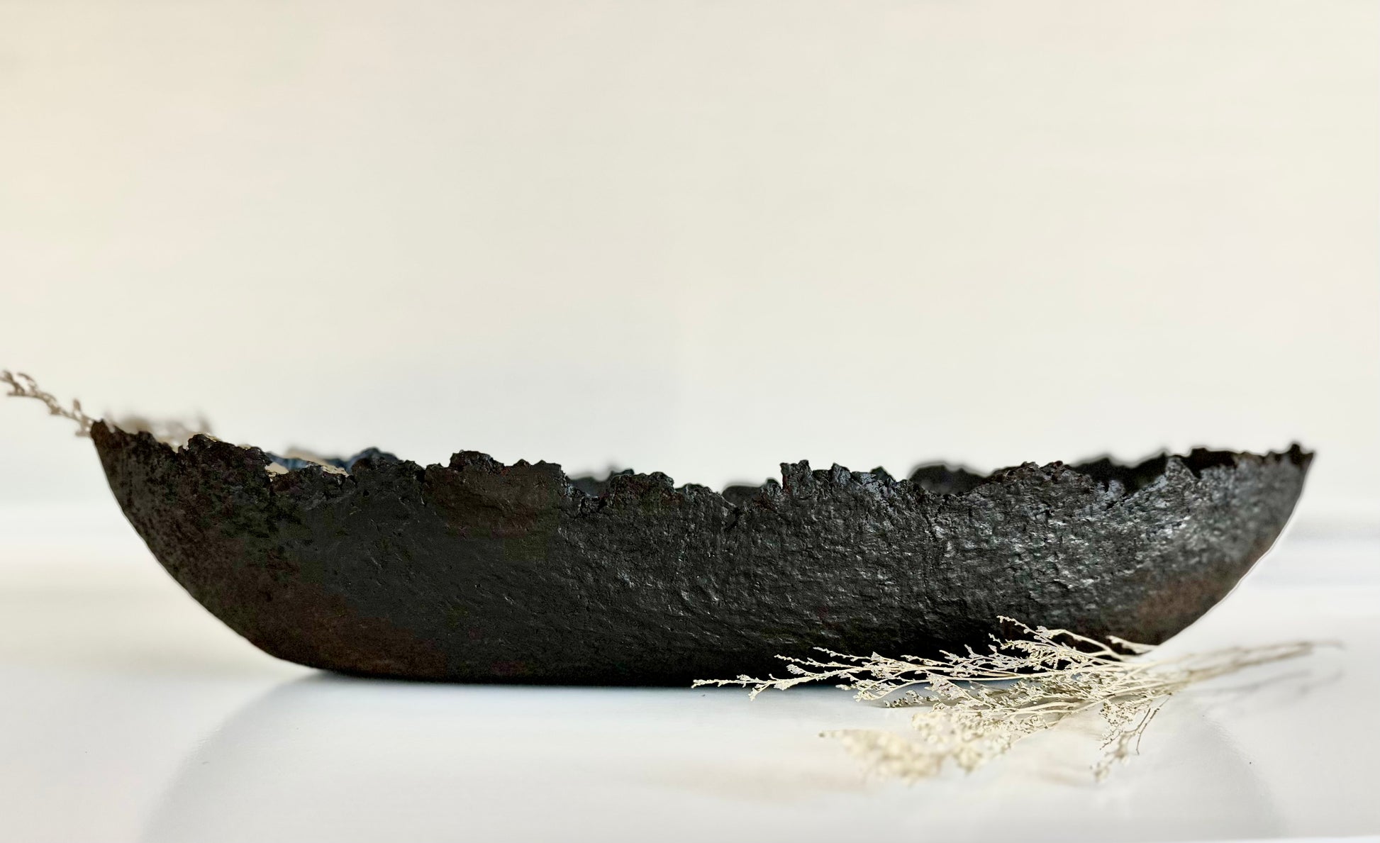 Oblong black textured decorative bowl with irregular edges on white surface. Handmade Paper Mache design by Artist Tam M Olson