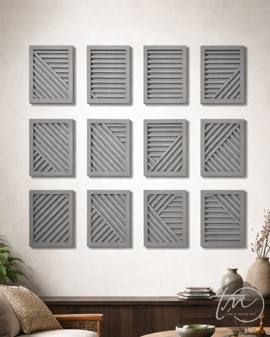 Twelve gray geometric wall art panels on a white wall above a wooden console table. Original Commercial Art by Tam M Olson