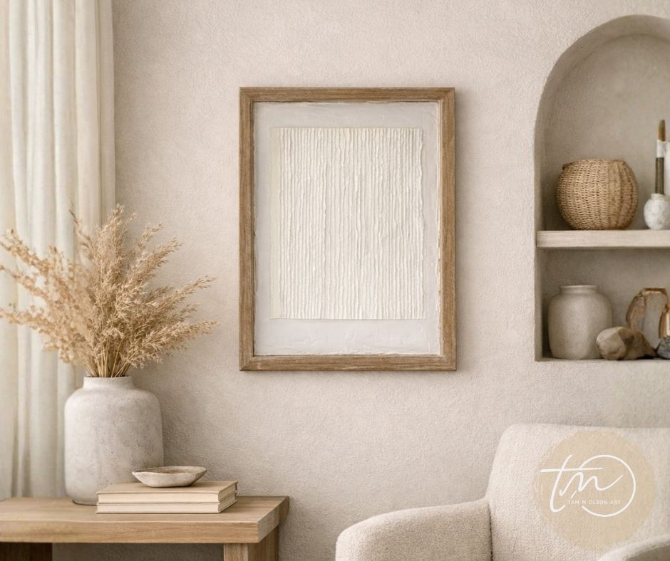White textured art in a wooden frame against a white wall in a cozy seating area with neutral decor. Original abstract art by artist Tam M Olson