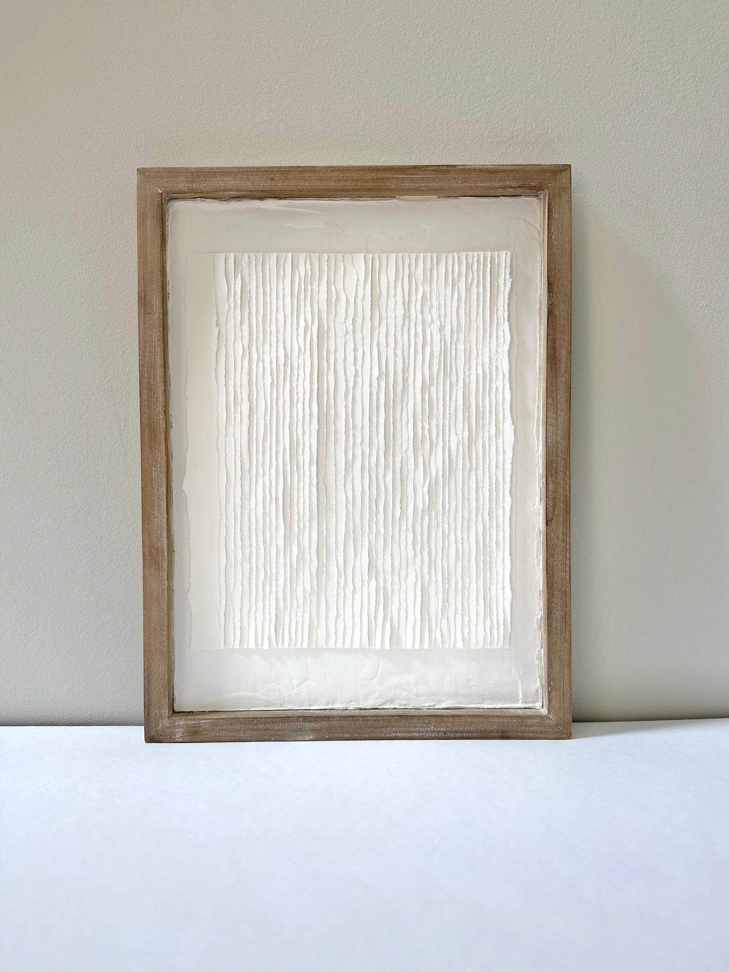 White textured art in a wooden frame against a white wall. Original abstract art by artist Tam M Olson