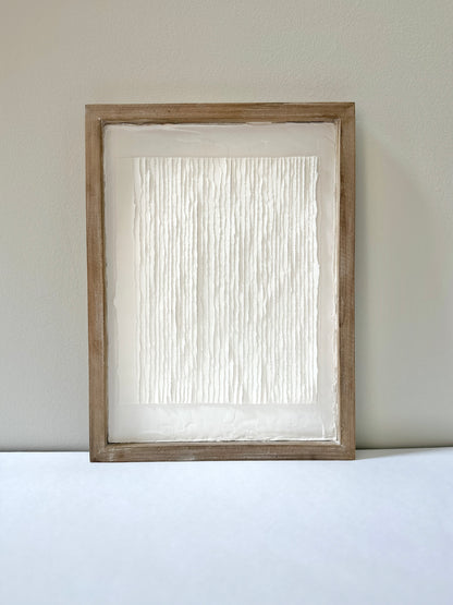 White textured art in a wooden frame against a white wall. Original abstract art by artist Tam M Olson