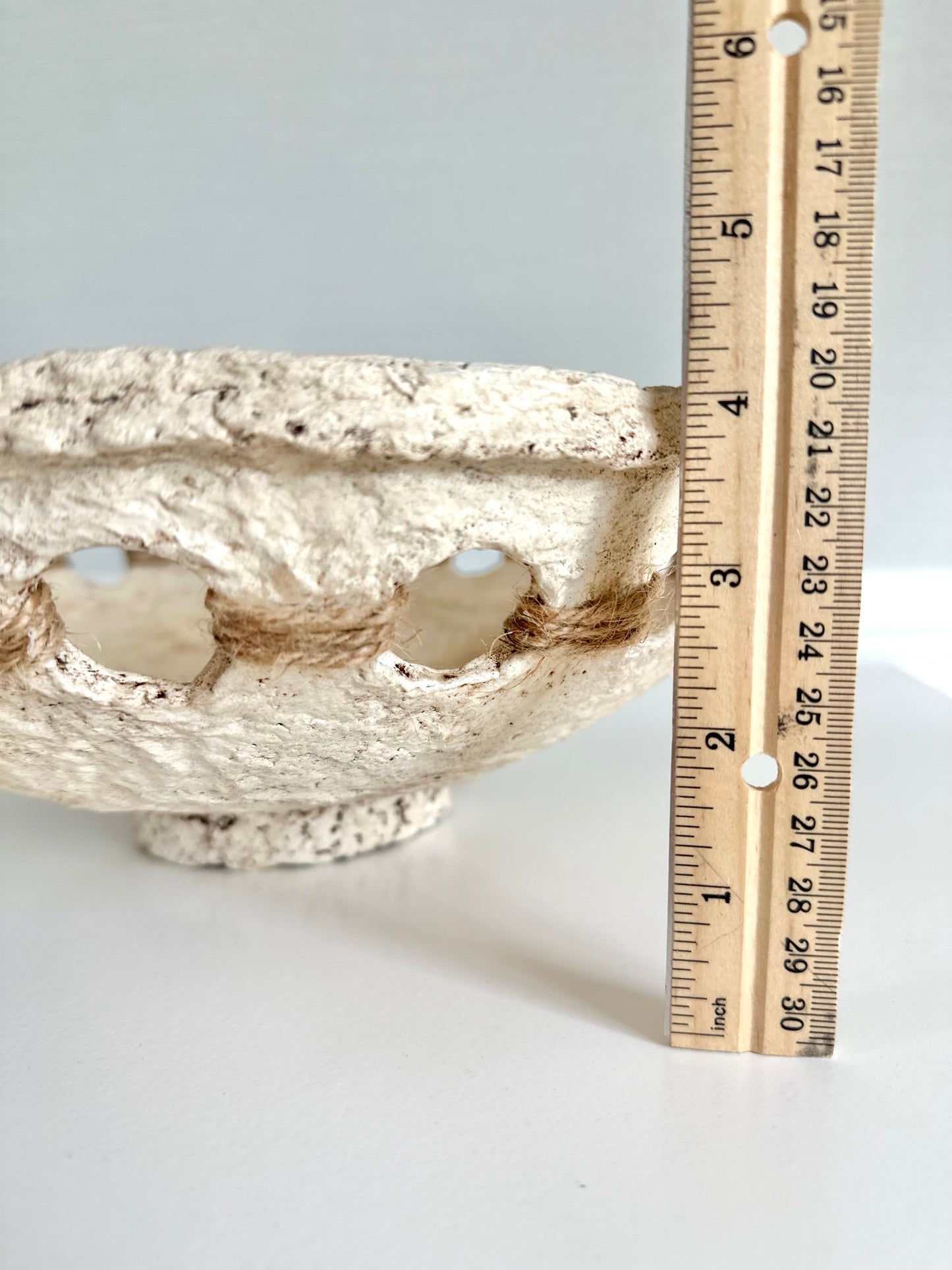 A beige, primitive handmade paper mache bowl with jute string accents on the side, placed on a flat surface. Displays bowl height of 4 inches. Designed by Artist Tam M Olson.