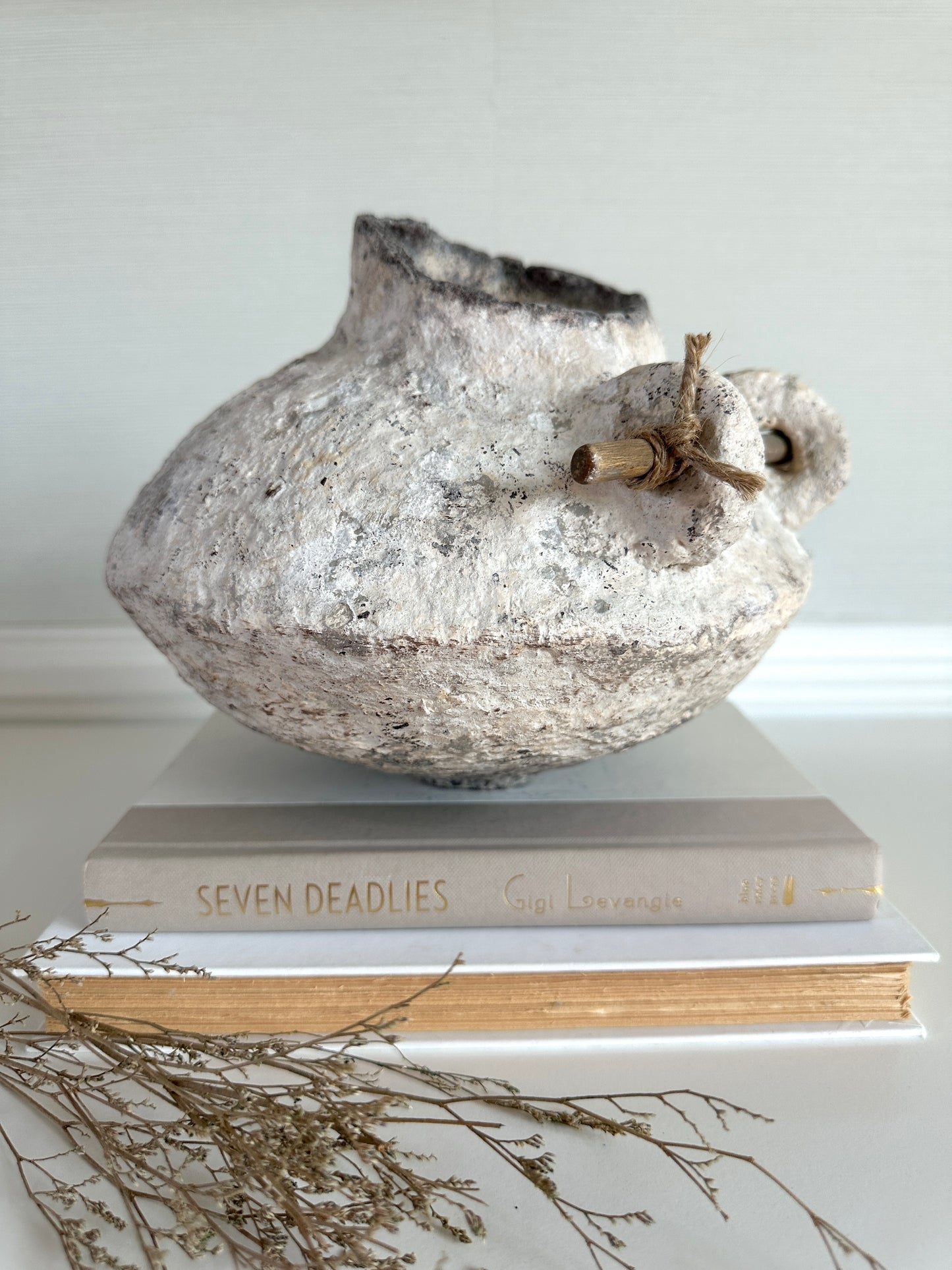 Decorative white rustic vase on top of books with a white background. Handmade by artist Tam M Olson