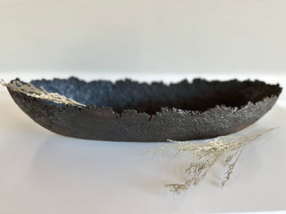 Oblong black textured decorative bowl with irregular edges on white surface. Handmade Paper Mache design by Artist Tam M Olson