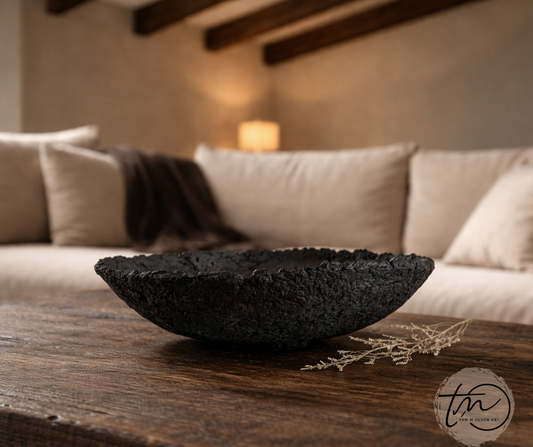 A rustic black decorative bowl made with paper mache, displayed on rustic coffee table in an earthy living room Designed by Artist Tam M Olson.