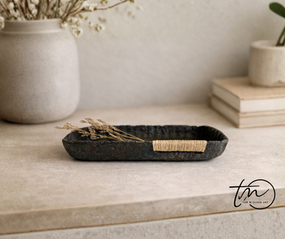 A small black decorative tray with a textured surface, made from paper mache, displayed on a table with other decorative objects. Original art by artist Tam M Olson