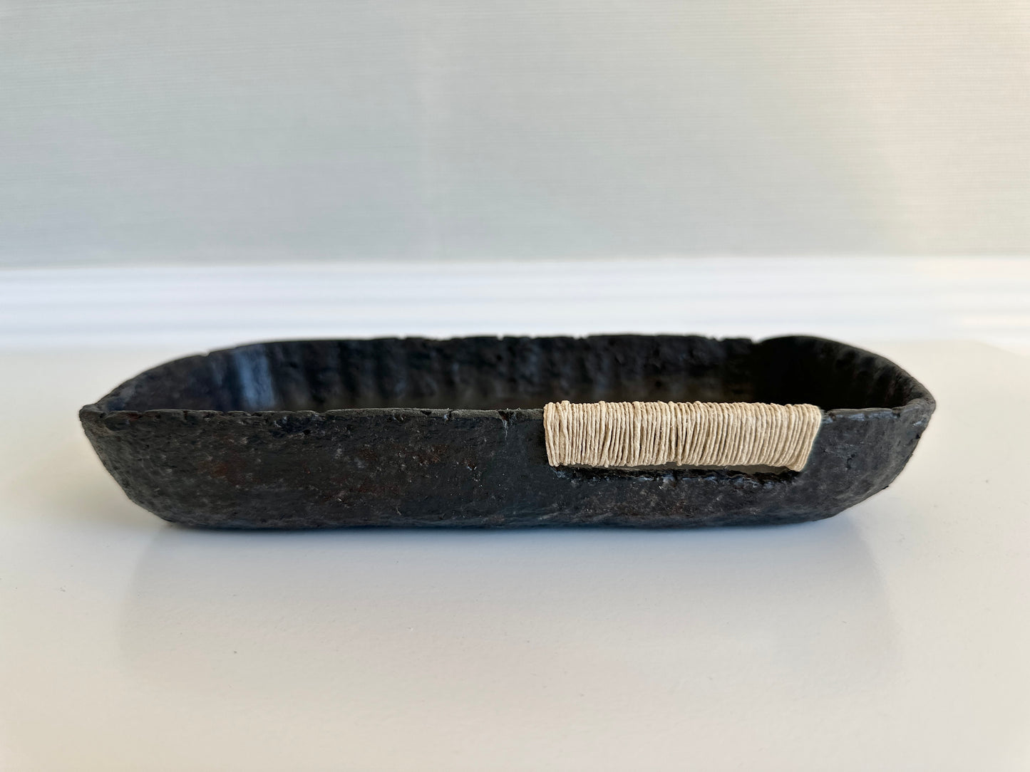 A small black decorative tray with a textured surface, made from paper mache, with jute string detail. Original art by artist Tam M Olson