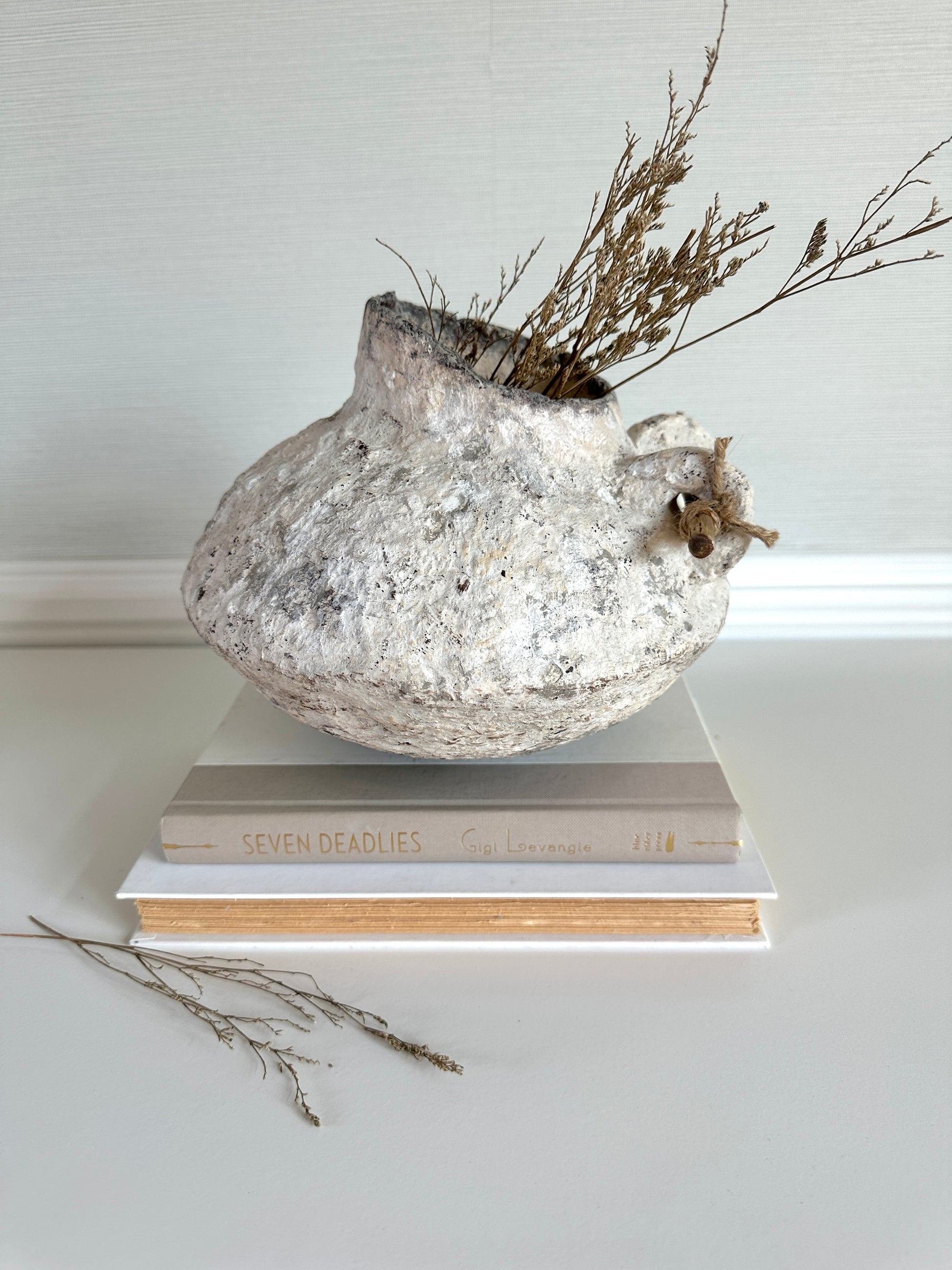 Decorative vase on books with dried plants against a light background. Handmade vase by artist Tam M Olson