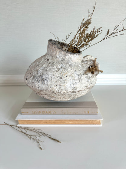 Decorative vase on books with dried plants against a light background. Handmade vase by artist Tam M Olson