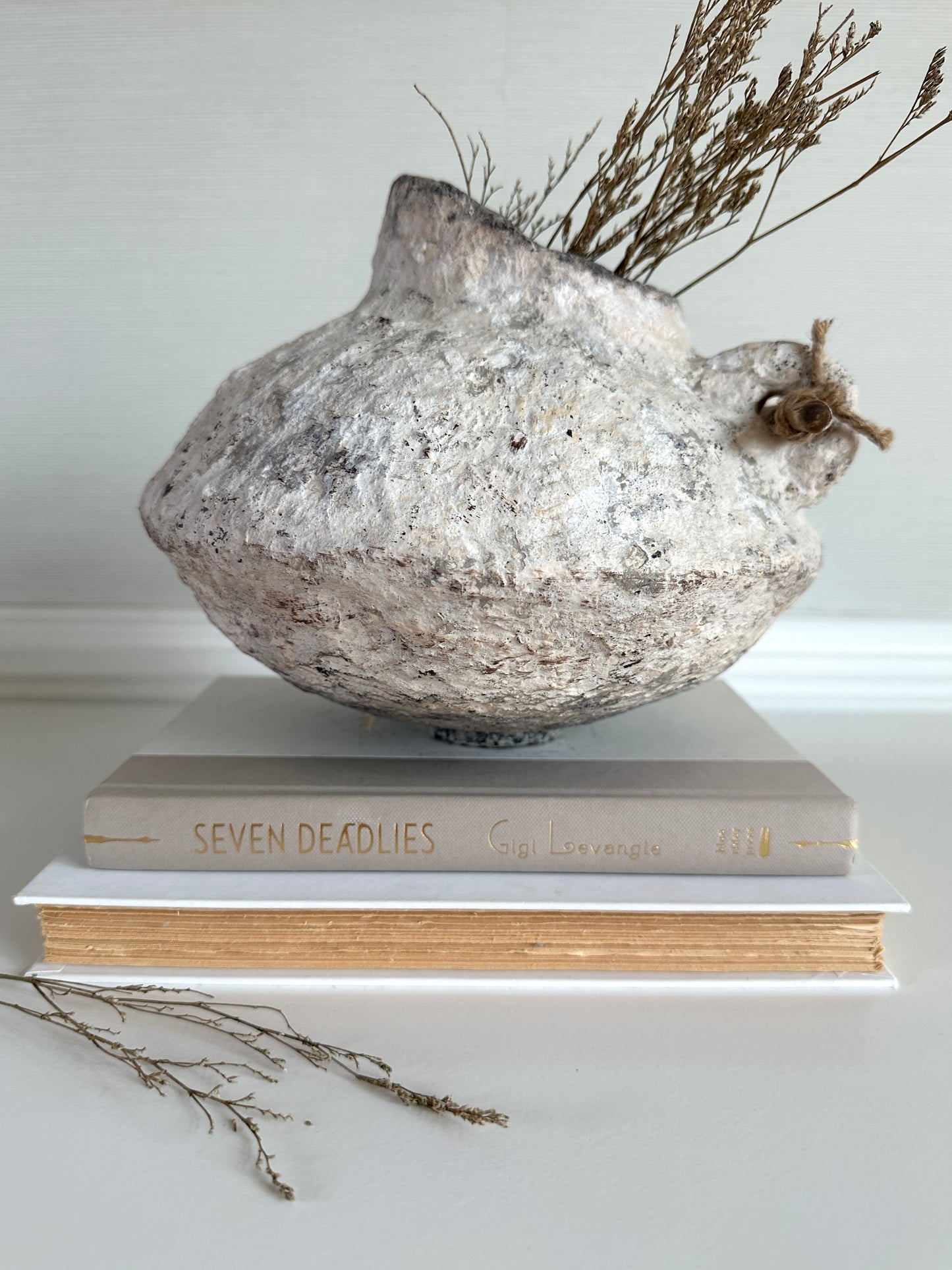 Decorative papier mache sculpture on top of books with dried plants on a neutral background. Original handmade design by artist Tam M Olson