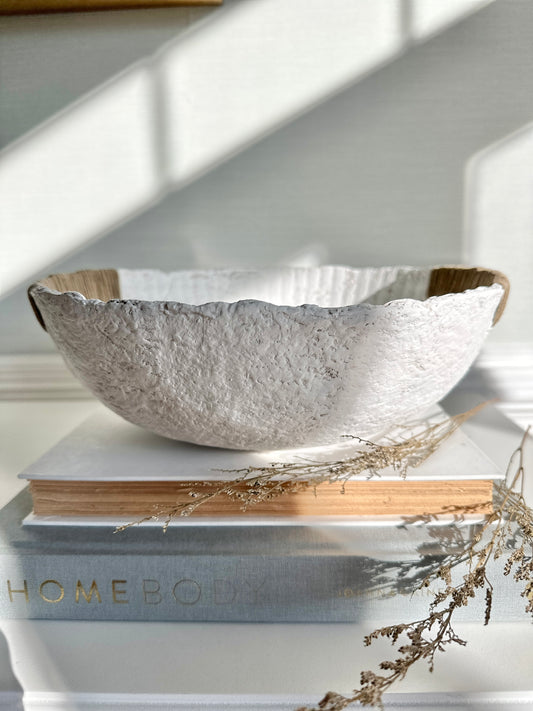 Handmade white paper mache bowl with hemp twine handles, displayed on top of books with a few dried flowers to show scale and use as a decorative object. Designed by Artist Tam M Olson.