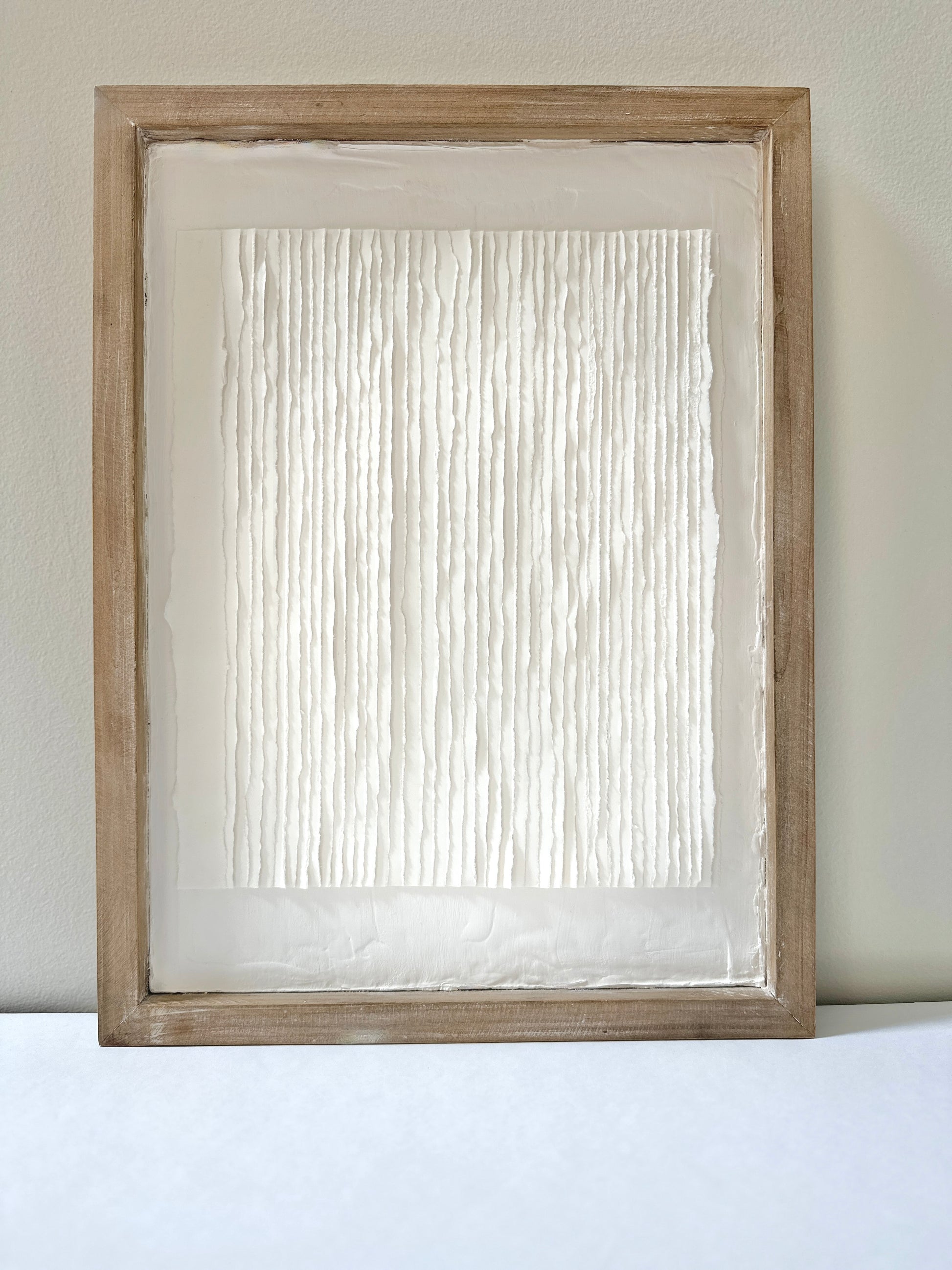 White textured art in a wooden frame against a white wall. Original abstract art by artist Tam M Olson