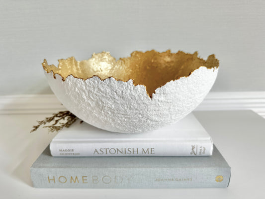 White Decorative textured bowl with gold interior and irregular edge made with paper mache material placed on stacked books. Original bowl handmade by artist Tam M Olson