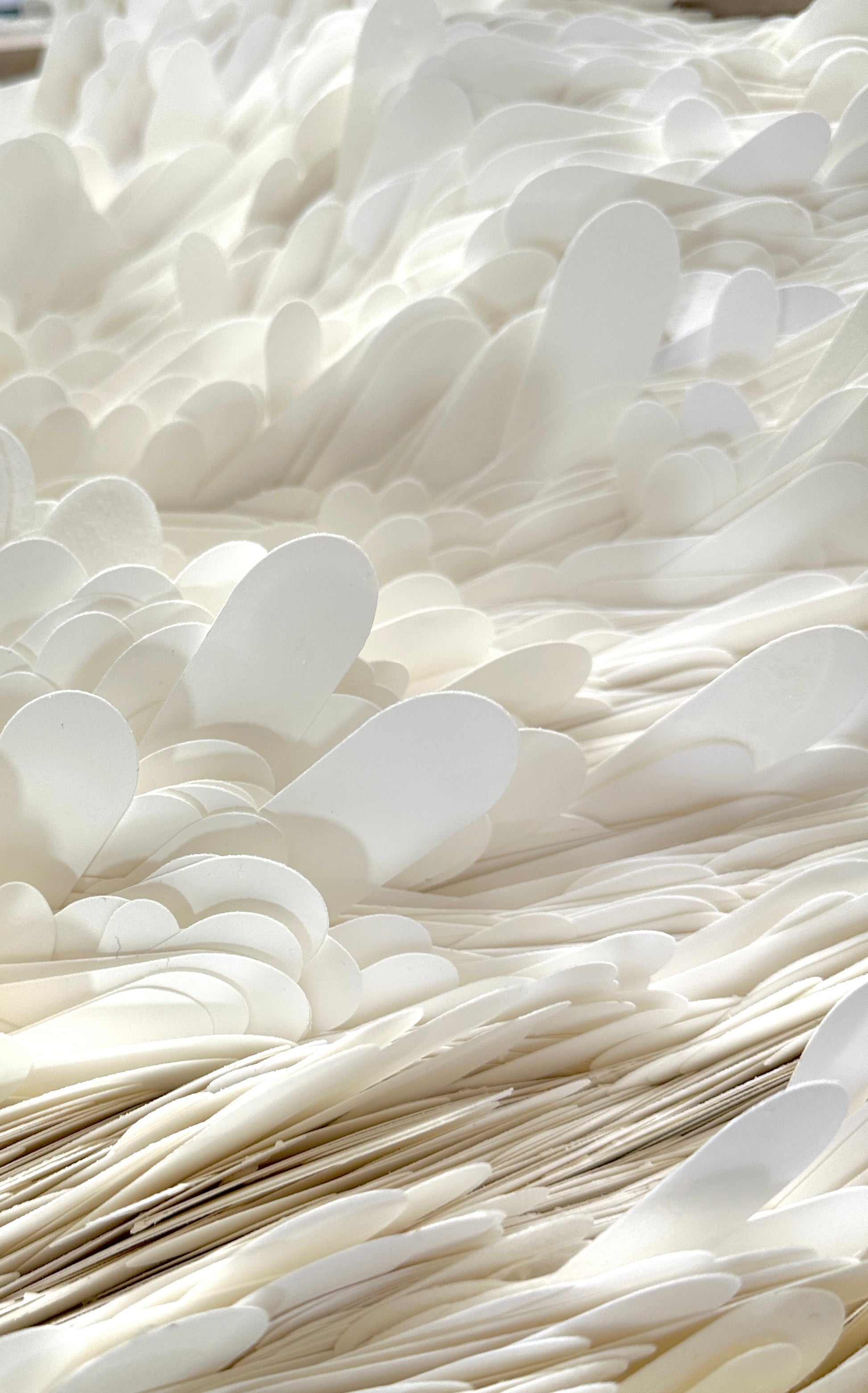 A close-up view of a large quantity of white cardstock fins stacked and layered together, filling the entire frame. Original art by Artist Tam M Olson