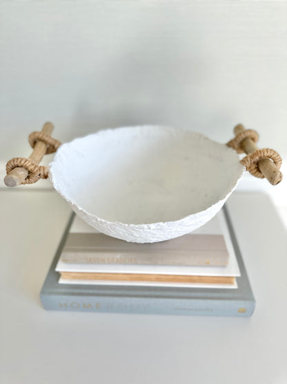 A handmade white paper mache bowl with driftwood and jute handles as a decorative item, placed on a stack of books. Designed by Artist Tam M Olson.