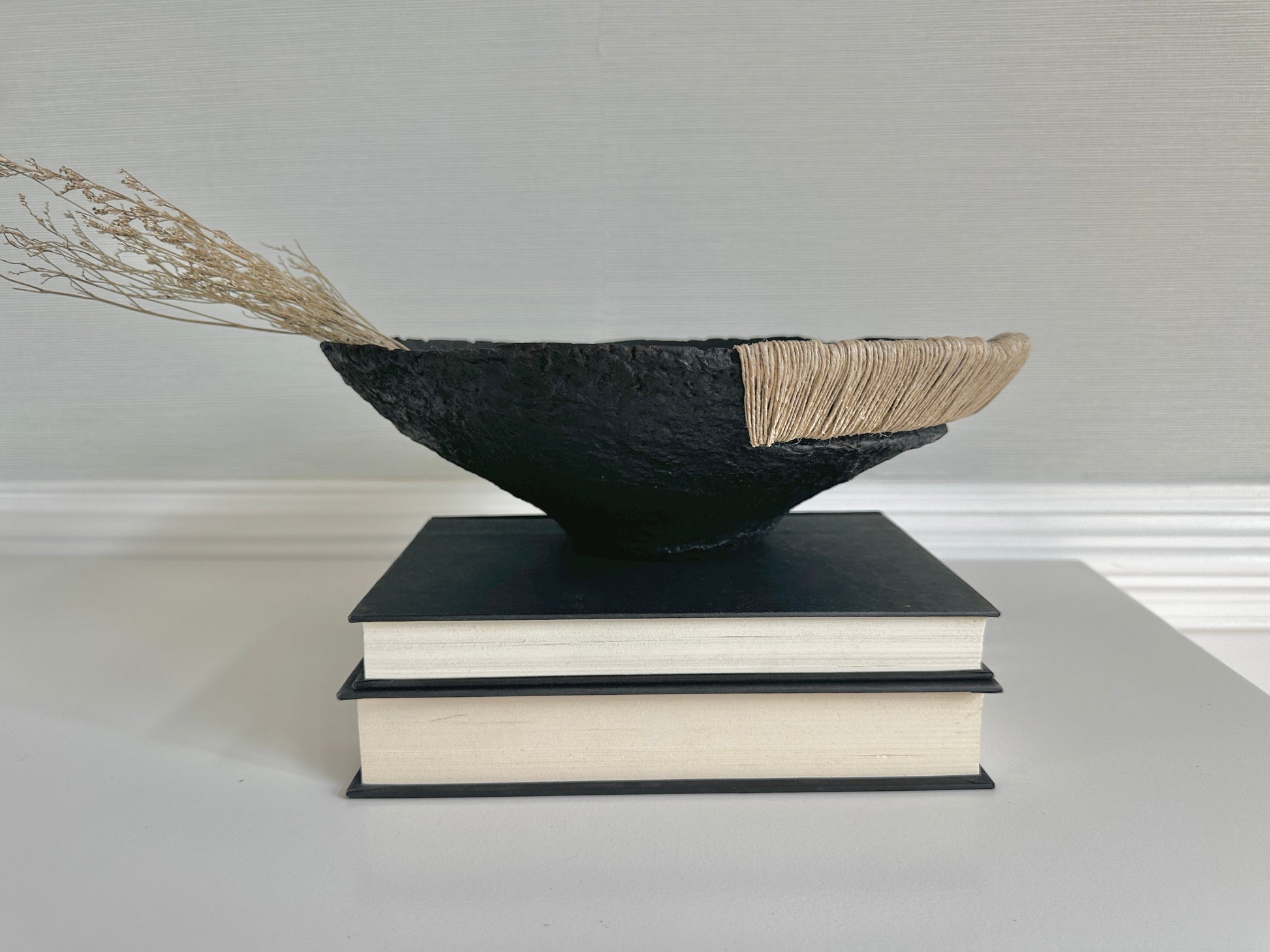 Decorative Black Bowl with Jute Twine and Wide Disposition on top of a small stack of books. Hand Made Paper Mache Bowl by Artist Tam M Olson.