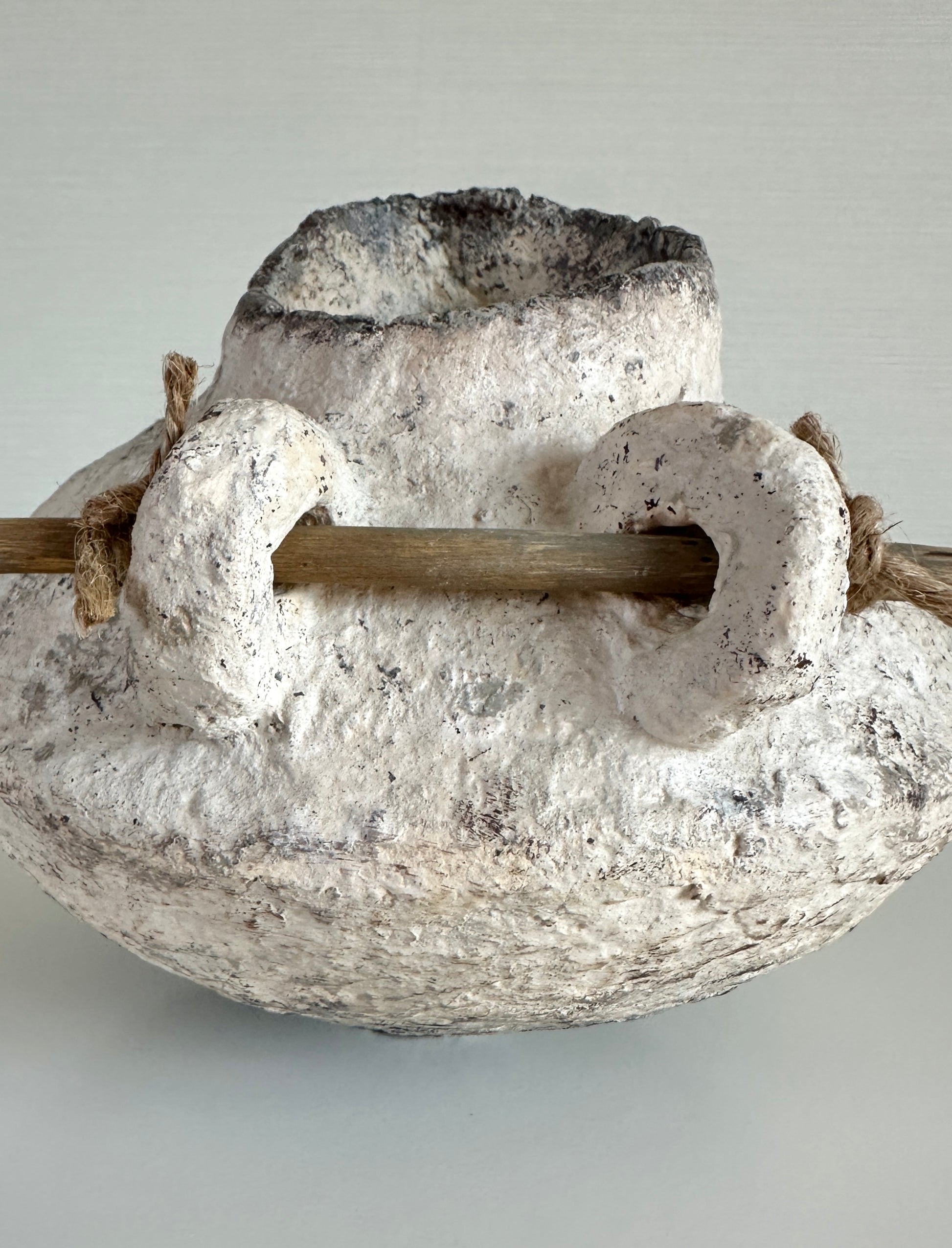 Decorative organic pitcher with a central wooden rod on a light gray background handmade by artist Tam M Olson